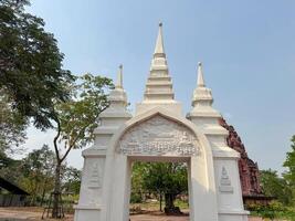 A white gateway stands tall amidst lush greenery near an ancient structure photo
