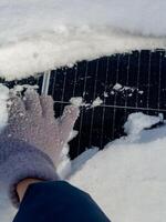 Hand clearing snow from a solar panel in winter while ensuring it remains functional for energy collection photo