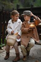 a boy and girl dressed in vintage clothing sit on an old wooden bench a lantern glowing softly in their hands photo