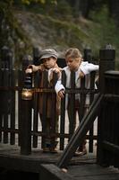dressed in old fashioned clothes a boy and girl stand on a rustic wooden bridge with a light in hands photo