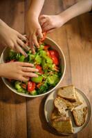 A colorful salad with fresh vegetables and crunchy croutons is surrounded by tiny reaching hands. photo