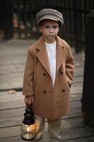 A child in old-fashioned attire stands with a lantern, like a character from the Victorian era, immersed in an atmosphere of mystery. photo