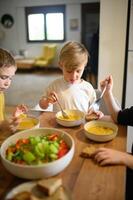Children eat soup at the table while a fresh salad sits in front of them, ready to be shared. photo