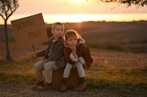 Dressed in vintage outfits, the kids sit on a worn suitcase, bathed in golden light. They gaze into the distance, hoping for someone to take them to the North Pole. photo