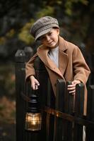 A boy in a vintage coat and hat holds a lantern, his face illuminated by its warm glow as darkness gathers around him. photo