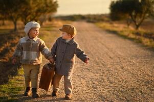 Two boys in vintage clothing stand on the road with a worn suitcase, looking into the distance, waiting for a ride. photo