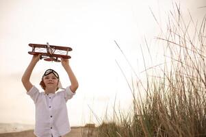 A young boy in a pilots hat holds a toy airplane high against the sunset sky, his eyes filled with dreams of adventure and flight. photo