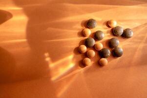 Medical supplements in the form of round tablets lie on an orange background. Tablets are round in shape. They are made of herbs of brown and orange color. Concept of natural medicine. photo