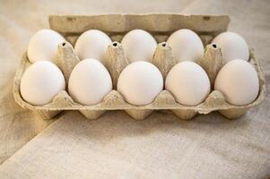 A chicken egg in a box. Meal. Easter. Black top viewbackground. High quality photo. egg carton on wooden table with linen tablecloth. eggs are white. photo