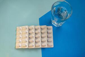 Medical pills in a blister and a glass of water on a blue background. Five white blisters with capsules lie in a row. There is a transparent glass with clean water. concept of medicine and treatment photo