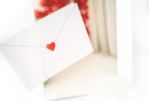 craft envelope made of white paper with a small cute heart. the envelope is located on the background of the interior, white and red, horizontal photo
