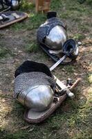 The knight's iron armor lies on the ground. The shield, chain mail, iron gauntlets, weapons of war, and helmet lie on the ground photo