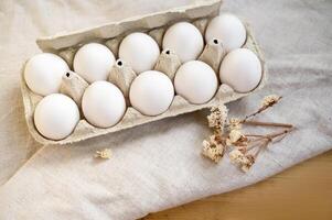 white eggs in a cardboard box, 10 pieces, on a surface made of natural materials.. A chicken egg in a box. Meal. Easter. light background. egg carton on wooden table with linen tablecloth photo