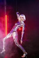 Blonde as a cyber robot. Girl in shining silver armor in neon. She stands in a glowing cube, red smoke around. Blonde with fantastic makeup and image in a dark key and colored light photo