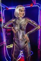 blonde as cyber robot. Girl in shining silver armor in neon. Blonde with fantastic makeup and image in dark key and color light, posing in cyberspace. screens and wires glow around. photo