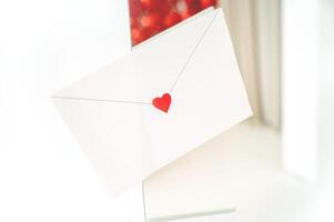 craft envelope made of white paper with a small cute heart. the envelope is located on the background of the interior, white and red, horizontal photo. photo