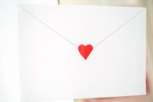 craft envelope made of white paper with a small cute heart. the envelope is located on the background of the interior. horizontal photo. photo