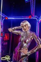 blonde as cyber robot. Girl in shining silver armor in neon. Blonde with fantastic make-up and image in dark key and color light, posing in cyberspace. screens glow around photo
