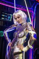 Blonde as a cyber robot. Girl in shining silver armor in neon. Blonde with fantastic makeup and image in dark key and colored light, posing in cyberspace. her hands are wrapped with a wire that glows photo
