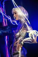 Blonde as a cyber robot. Girl in shining silver armor in neon, Blonde with fantastic makeup and image in dark key and colored light, posing in cyberspace. her hands are wrapped with a wire that glows. photo