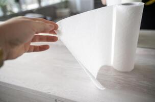 A white paper towel stands on a wooden table. A woman holds it. There is a mirror nearby. The towel is unfolded. photo