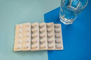 Medical pills in a blister and a glass of water on a blue background. Five white blisters with capsules lie in a row. Transparent glass with clean water. Concept of medicine and treatment photo
