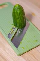 Fresh green cucumber on a light green mandoline slicer, ready for slicing . High quality photo