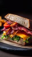 A towering rye sandwich overflowing with layers of crispy bacon, fresh tomato slices, sharp cheese, and crisp lettuce, wrapped in paper with a dark, moody background. . photo