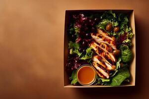 A grab-and-go salad in a cardboard box with grilled chicken, fresh lettuce, black and green olives, and a side of rich dressing, set on a warm brown background. . photo