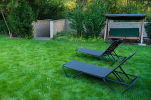Peaceful backyard featuring two garden loungers and a swing bench set on a lush green lawn photo
