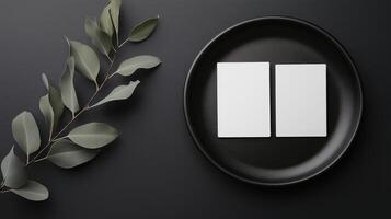 Two blank business cards on a black plate with eucalyptus leaves photo