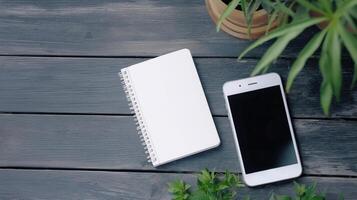 White notebook and smartphone on wooden table with potted plants photo