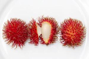 Close up of fresh rambutan fruits growing in southern Asia with red hairy skin, juicy pulp in the middle isolated on white background photo