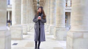 Girl in Gray Coat Walking with Coffee Between Columns in Paris, Camera in Motion video