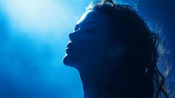 Woman gazes upwards, illuminated by vibrant blue light, creating a serene and ethereal atmosphere. Mysterious beauty. photo