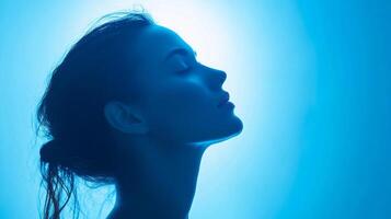 Serene beauty illuminated in calming blue hues, epitomizing tranquility and inner peace, with closed eyes and upward gaze into light. photo
