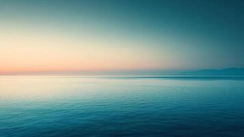 A serene seascape featuring a calm ocean reflecting a gradient sky at dusk, with distant mountains adding depth to the tranquil scene. photo