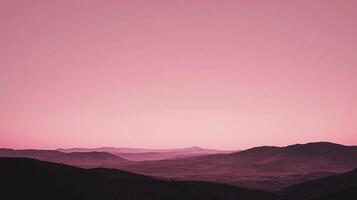A serene, pink-hued landscape of silhouetted mountains against a soft gradient sky evokes tranquility and natural beauty. photo