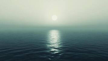 A serene, atmospheric view of the sea at sunset. The sun reflects off the water, creating a tranquil and calming ocean scape. photo