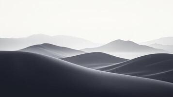 Monochromatic desert scene with undulating sand dunes, rendered in shades of gray against a bright, hazy sky and distant mountain range. photo