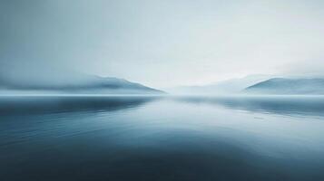 Serene view of calm water reflecting a mountain range shrouded in mist on the horizon in soft, muted blue tones, exuding peace. photo