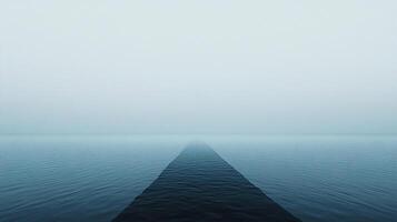 Serene ocean fading into a misty horizon, minimalist and calm, showcasing vastness and tranquility. The water surface is still and blue. photo