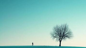 Lone figure by a bare tree against a serene cyan sky, evoking solitude and contemplation in a minimal landscape. Nature's simplicity. photo