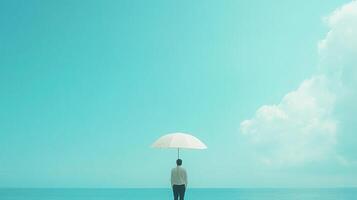 A person with an umbrella gazes out at a serene blue ocean, meeting a cloud-filled sky on a sunny day, creating a tranquil, picturesque scene. photo