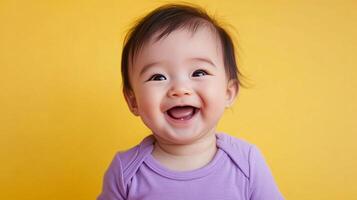 Adorable Asian baby bursts with joy, showcasing a beaming smile against a vibrant yellow backdrop. A picture of innocence, joy, and charm. photo