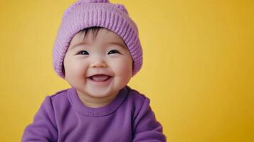 Adorable baby smiling brightly with a purple beanie and matching shirt against a vibrant yellow backdrop, radiating pure joy and innocence. photo