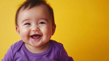 A cheerful baby with an open mouth and gleaming eyes radiates pure joy in front of a vibrant yellow backdrop, evoking feelings of happiness. photo