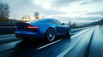 A blue sports car speeds along a wet highway under a cloudy sky, showcasing speed and modern design in a scenic environment. photo