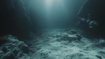 Underwater scene with dim light filtering down. Rocky terrain and sediment-covered floor. Depth is evident with limited visibility. photo