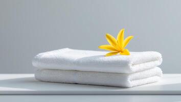 White towel is laying on a table with a yellow flower on top of it photo